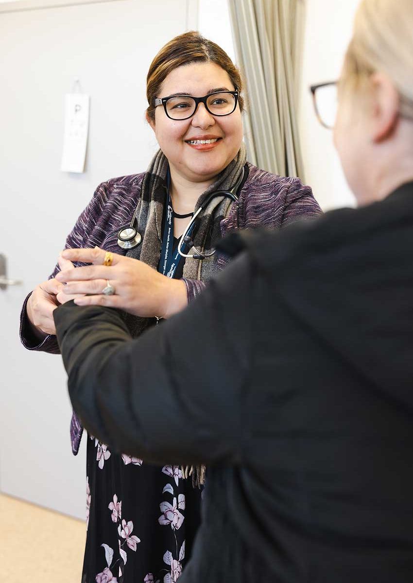 A female doctor, smiling, checks the heart rate of her patient.